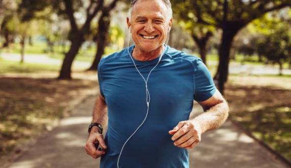 An elderly man is jogging and smiling, he is listening to music as he exercises