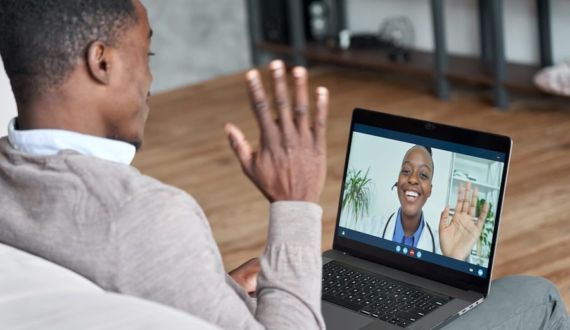 Male black patient talking on conference video call to female african doctor. Virtual therapist consulting young man during online appointment on laptop at home. Telemedicine chat, telehealth meeting stock photo